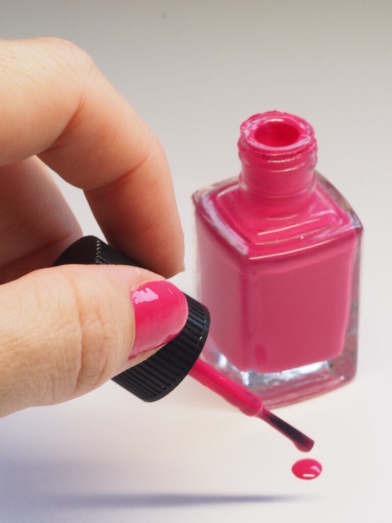 Mão segurando pincel de um esmalte rosa.