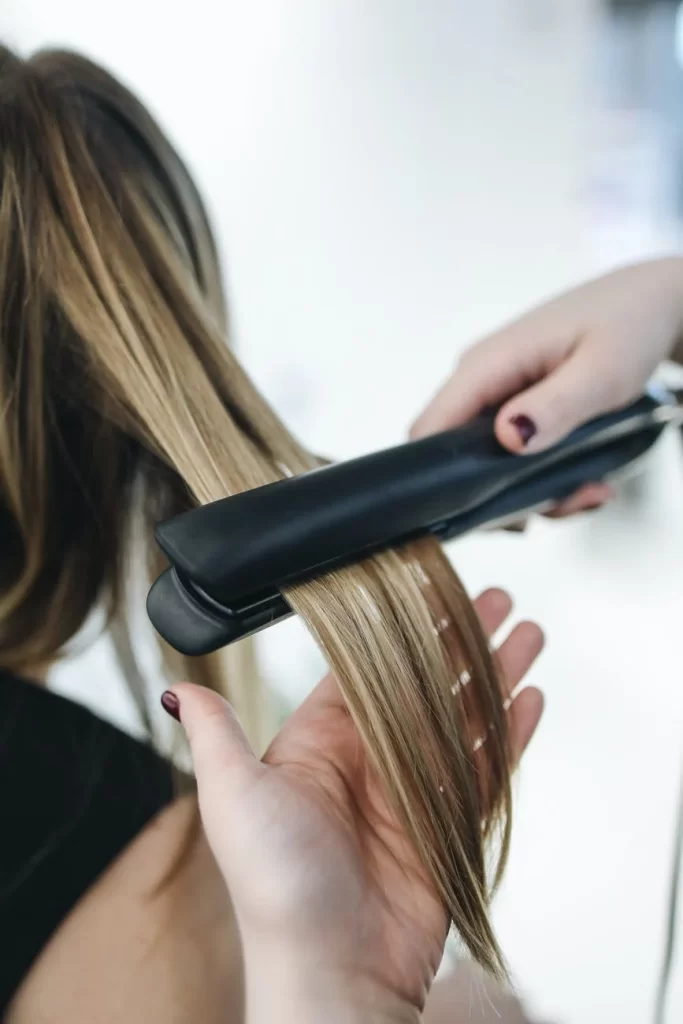 Pessoa passando chapinha no cabelo de uma mulher loira.